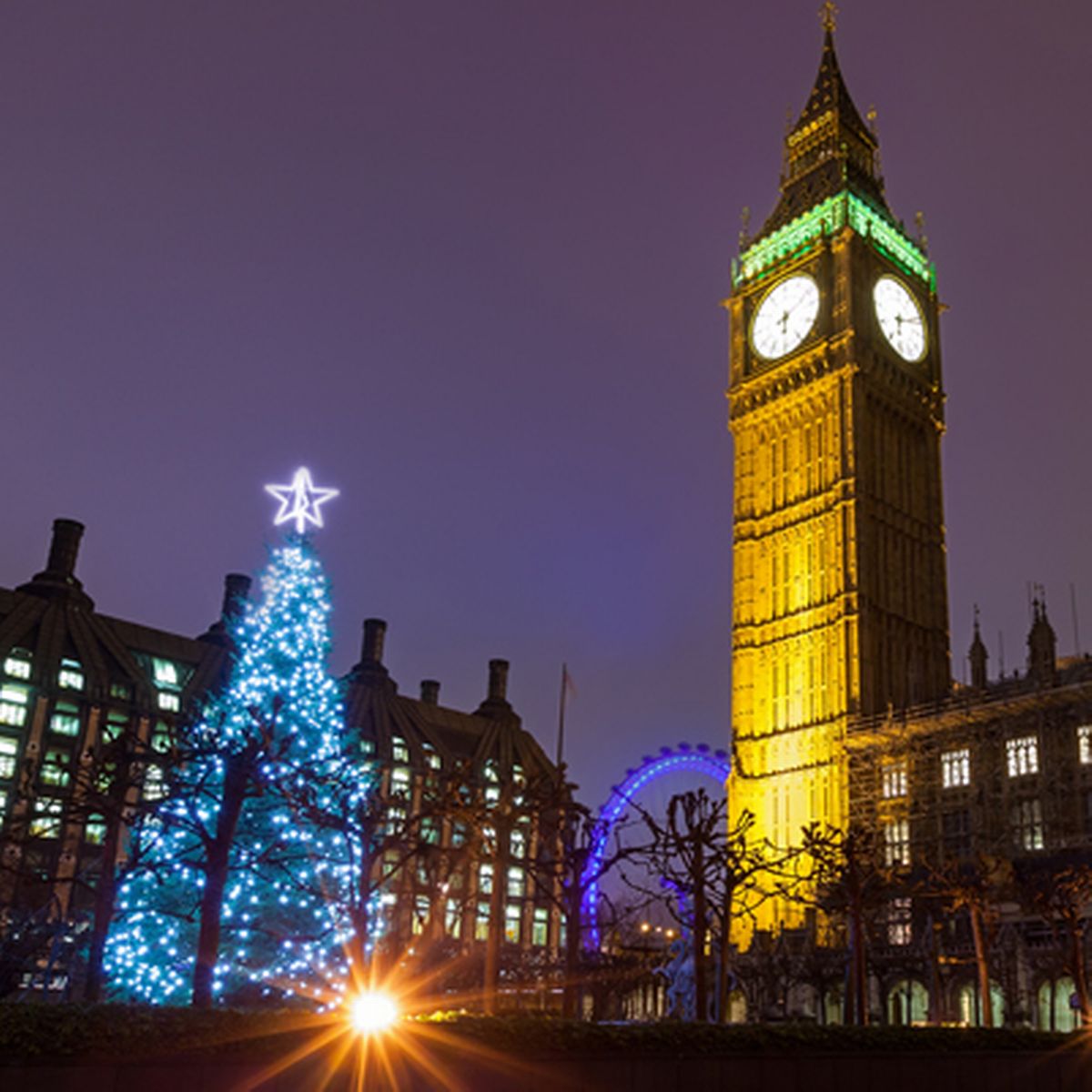 big ben lit up in front of dark night sky christimas tree with blue lights